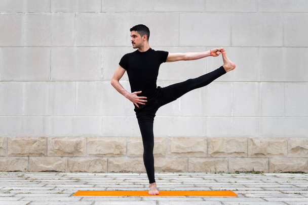 Розширена рука до позу великого нога. Привабливий латинський чоловік робить йогу на відкритому повітрі в місті
. - Фото, зображення