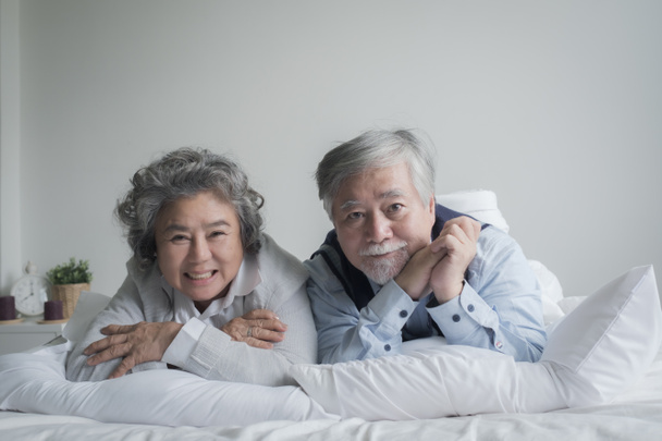 ηλικιωμένο ζευγάρι καυκάσιος ηλικιωμένος άνδρας και γυναίκα κοιμούνται στο κρεβάτι και χαμογελώντας σε λευκή κουβέρτα στο υπνοδωμάτιο, συνταξιοδότηση υγειονομική περίθαλψη με την έννοια του τρόπου ζωής αγάπη - Φωτογραφία, εικόνα
