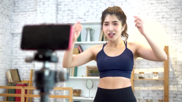 20s young Asian woman in sportswear doing talking to camera and explaining fitness tutorials online. Healthy girl blogger in living room at home. Teaching online bodybuilding class concept - 映像、動画