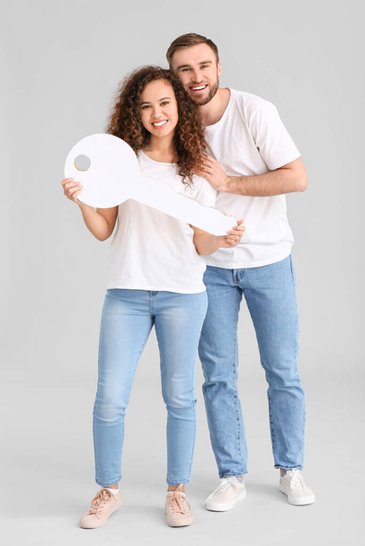 Glückliches junges Paar mit großem Papierschlüssel auf grauem Hintergrund - Foto, Bild