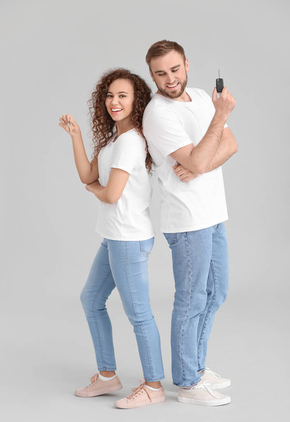Young couple with key from car and home on grey background - Photo, Image