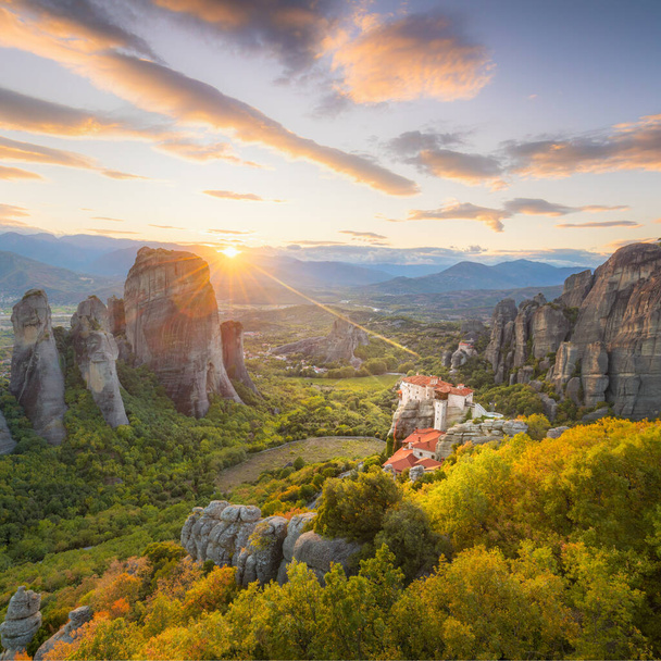 Landscape of Meteora, Greece at romantic sundown time with real sun and sunset sky. Meteora - incredible sandstone rock formations.  The Meteora area is on UNESCO World Heritage - Фото, изображение