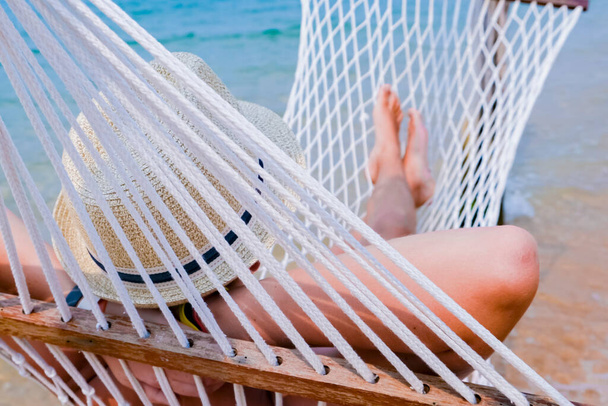 Boy with sandy feet lying in a hammock at the beach. Cozy hammock on the tropical beach by the sea. Copy space banner. - 写真・画像