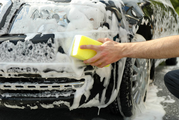 Facet wyciera samochód gąbką. Myjnia samochodowa. - Zdjęcie, obraz