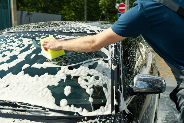 Ο άνθρωπος σκουπίζει το αυτοκίνητο με ένα σφουγγάρι. Καθαρίστε την έννοια του αυτοκινήτου - Φωτογραφία, εικόνα