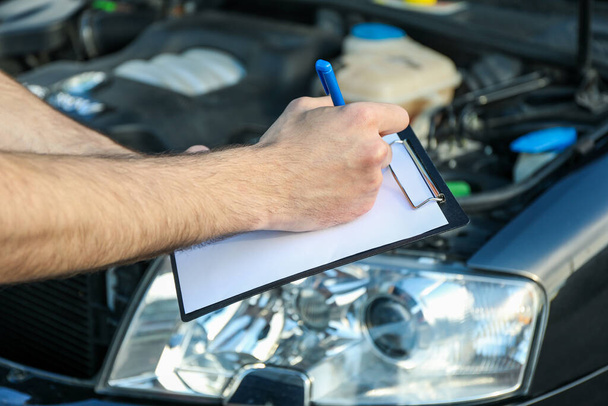 Ein Mann in Overalls schreibt an ein Klemmbrett. Mechaniker. Auto-Inspektion - Foto, Bild