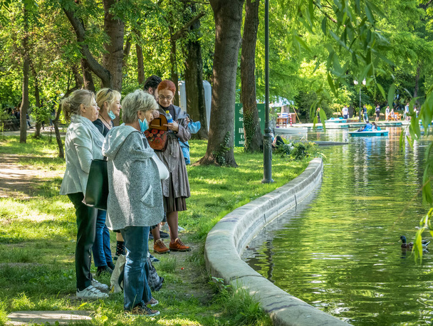 Βουκουρέστι / Ρουμανία - 05.30.2020: Ομάδα ηλικιωμένων στην άκρη μιας λίμνης που παρακολουθεί τις πάπιες. Γριές που χαλαρώνουν στο πάρκο Cismigiu. - Φωτογραφία, εικόνα