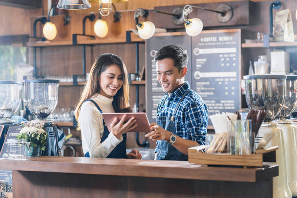 Владелец азиатского малого бизнеса беседует с коллегами и использует технологический планшет перед стойкой регистрации, предпринимателем и стартапом, готовясь к обслуживанию клиента в кафе-магазине Concep
 - Фото, изображение