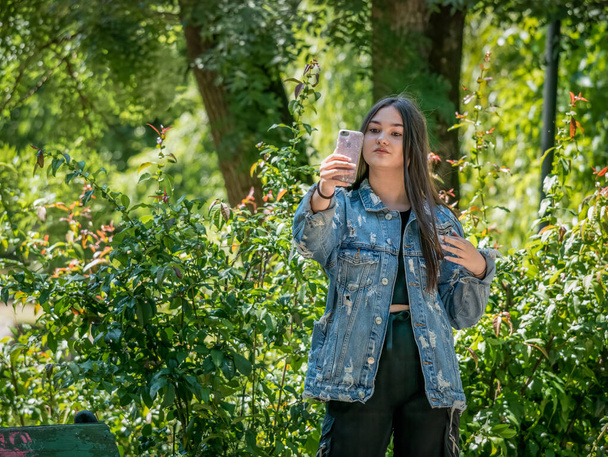 Bucarest / Romania - 30.05.2020: Giovane ragazza che si fa un selfie con lo smartphone. Ragazza al parco Cismigiu, a Bucarest. Concetto di dipendenza da smartphone
. - Foto, immagini