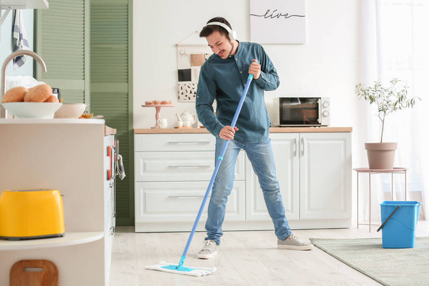 Handsome young man mopping floor in kitchen - Fotografie, Obrázek