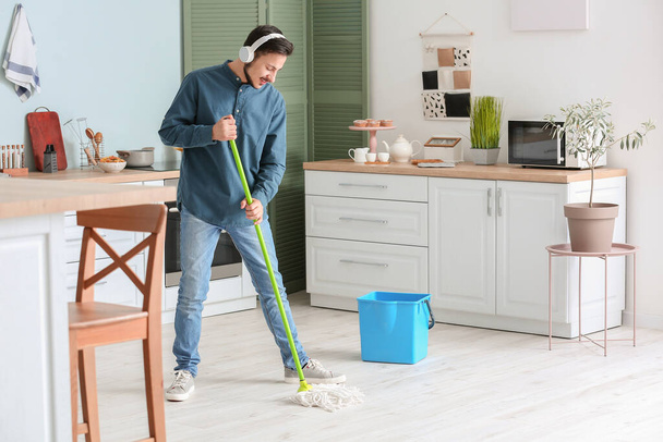 Handsome young man mopping floor in kitchen - Photo, Image