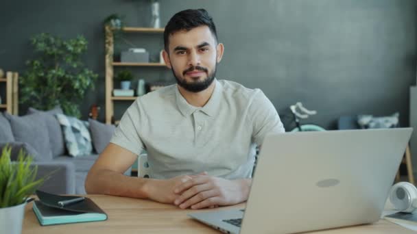 Slow motion portrait of Middle Eastern man at desk at home sitting alone and looking at camera - Video