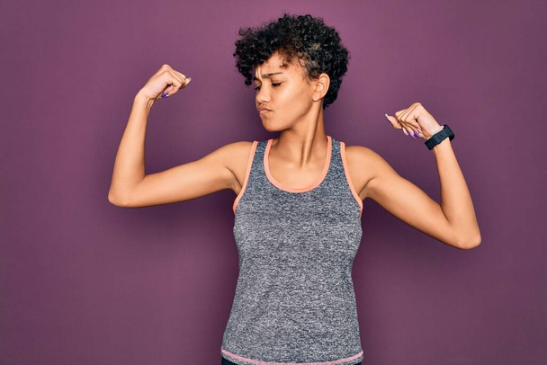 Young beautiful african american afro sportswoman doing exercise wearing sportswear showing arms muscles smiling proud. Fitness concept. - Photo, Image