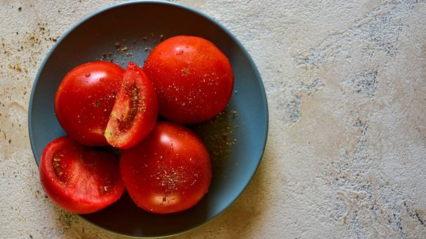 Plate with ripe tomatoes sprinkled with provencal herbs. Light textured background. Healthy tasty snack. Top view. Copy space. - Photo, Image
