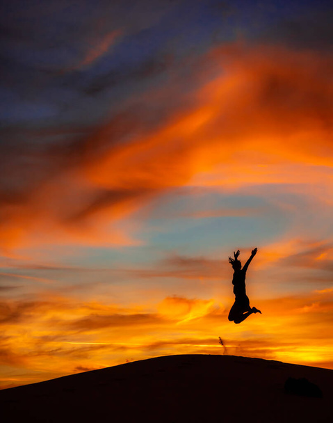 Jalapo, Brasil, 2018 - Mujer saltando con los brazos levantados sobre dunas de arena al atardecer
 - Foto, Imagen