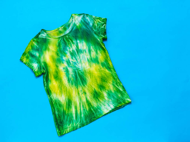 Yellow and green tie dye t-shirt on a bright blue background. Flat lay. - Photo, Image