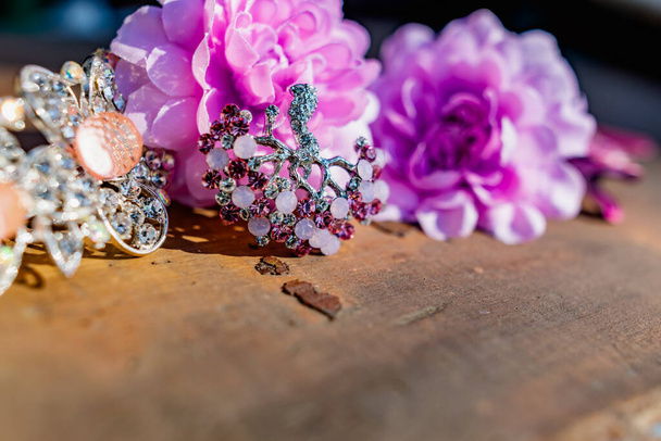 A composition of women's jewelry and accessories in pink on an old wooden surface. Brooch with colored stones, hairpins and flowers in delicate shades - Foto, afbeelding