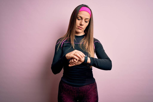 Young blonde fitness woman wearing sport workout clothes over isolated background Checking the time on wrist watch, relaxed and confident - Photo, Image