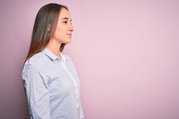 Молодая красивая деловая женщина в элегантной рубашке стоя на изолированном розовом фоне глядя в сторону, расслабиться профиль позировать с естественным лицом с уверенной улыбкой
. - Фото, изображение