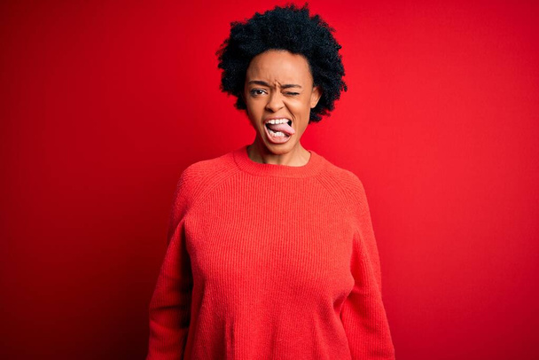 Young beautiful African American afro woman with curly hair wearing casual sweater sticking tongue out happy with funny expression. Emotion concept. - Foto, afbeelding