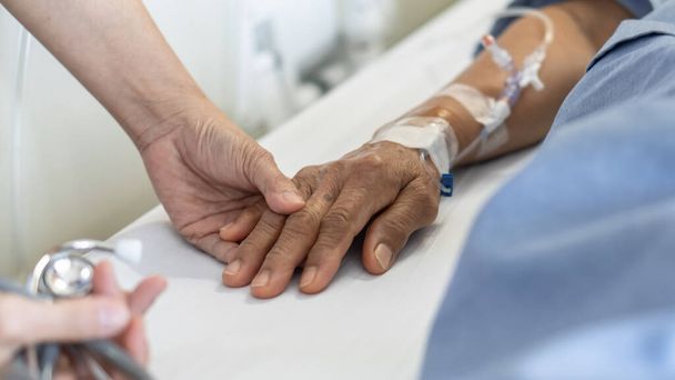 Elderly senior aged patient on bed with geriatric doctor holding hands for trust and nursing health care, medical treatment, caregiver and in-patient ward healthcare in hospital  - Photo, Image