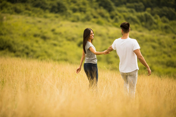 Szczęśliwa młoda para zakochana przechadzająca się po polu trawy w letni dzień - Zdjęcie, obraz