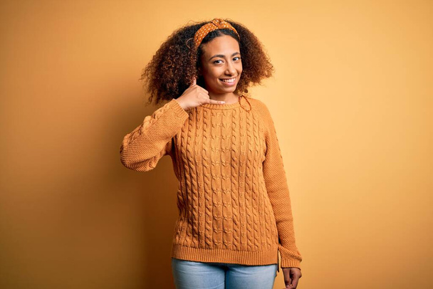 Afro saçlı, sarı arka planda rahat süveter giyen, el ve parmaklarıyla telefonla konuşan Afro-Amerikan genç bir kadın. İletişim kavramları. - Fotoğraf, Görsel