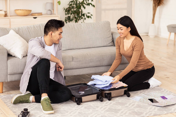 Young Couple Packing Suitcase For Vacation Sitting On Floor Indoors - Photo, Image