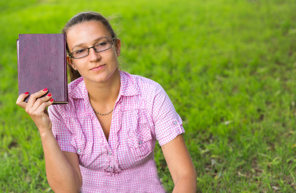 Woman holding a book on the grass background. - 写真・画像