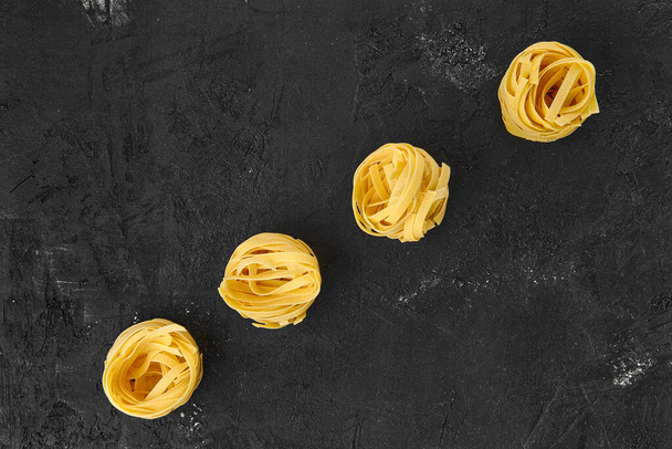 Top view of raw tagliatelle on black background - Foto, afbeelding