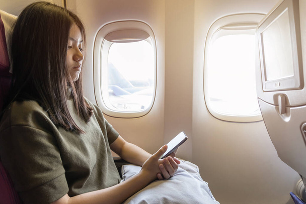 Tecnologia in volo che viaggia o vola in aereo con una giovane passeggera o viaggiatrice che utilizza smartphone, app online e Internet mentre è seduta sul sedile dell'aereo durante il viaggio - Foto, immagini