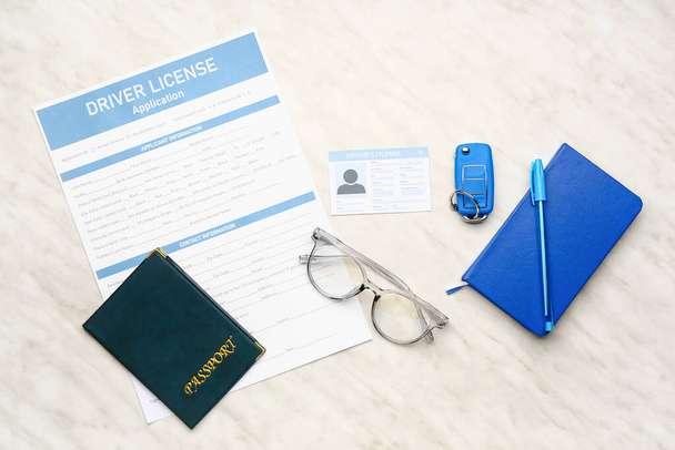 Licencia de conducir con formulario de solicitud, pasaporte, llave del coche y cuaderno sobre fondo blanco
 - Foto, Imagen