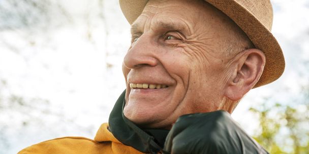 wrinkled pensioner in hat smiles against garden closeup - 写真・画像