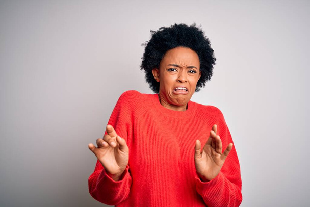 Young beautiful African American afro woman with curly hair wearing red casual sweater disgusted expression, displeased and fearful doing disgust face because aversion reaction. - Foto, immagini