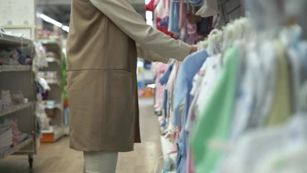 ouderschap, vrouwelijke klant in kinder kleding afdeling kiest dingen voor pasgeboren baby op planken van de winkel, close-up - Video