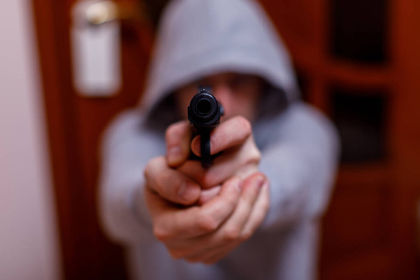 Man in hood with gun or pistol. Gangster, violence, outrage, force, rape or criminal concept, focus on the gun. - Photo, Image