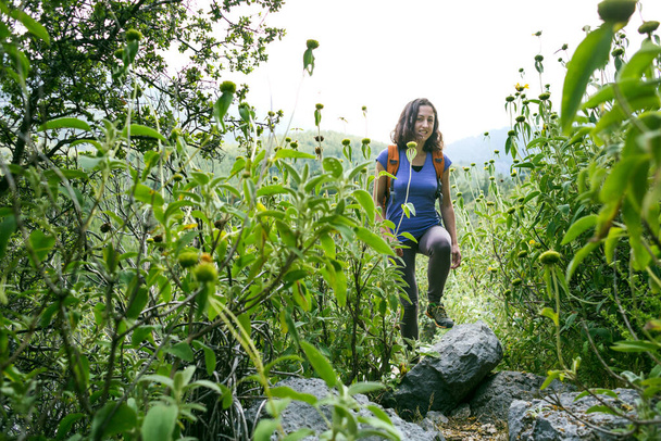 Een vrouw met een rugzak gaat langs het pad door het hoge gras, een meisje op een wandeling in de natuur na quarantaine, outdoor activiteiten. - Foto, afbeelding