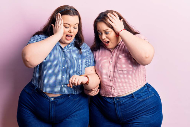 Young plus size twins wearing casual clothes looking at the watch time worried, afraid of getting late  - Foto, Imagem
