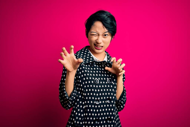 Joven hermosa asiática chica usando casual chaqueta de pie sobre aislado rosa fondo sonriendo divertido haciendo garra gesto como gato, agresivo y sexy expresión
 - Foto, imagen