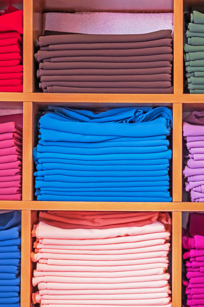 Ξύλινη ντουλάπα με διαφορετικά χρώματα ρούχα οθόνη στο κατάστημα ρούχων. - Φωτογραφία, εικόνα