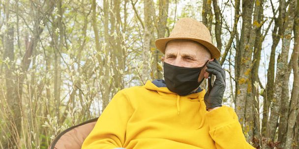 old man in black gloves and mask sits in garden closeup - Fotó, kép