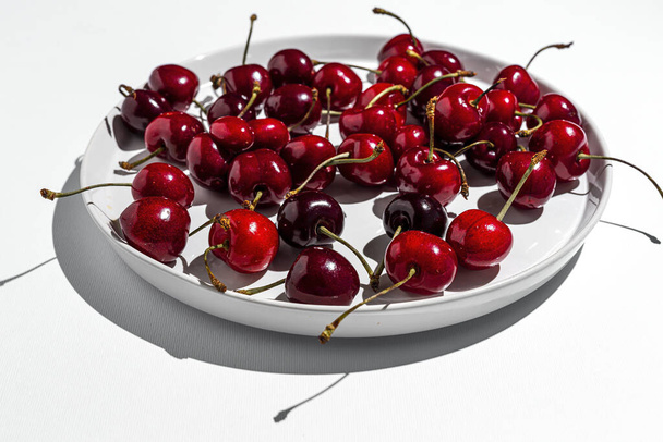 Fresh seasonal red cherries with strong sunlight on colored backgrounds - Foto, Imagem