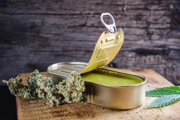 Marihuana knoppen. Medicinale cannabis boter in een open blik. hennepbladeren. horizontale oriëntatie. op houten ondergrond - Foto, afbeelding