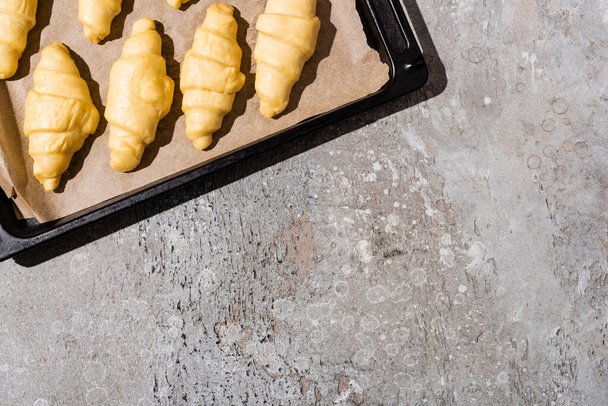 top view of uncooked croissants on baking tray on concrete grey surface - Foto, imagen