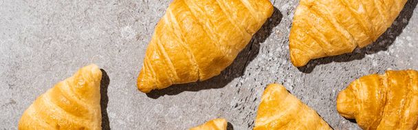 top view of fresh baked croissants on concrete grey surface, panoramic shot - Fotó, kép