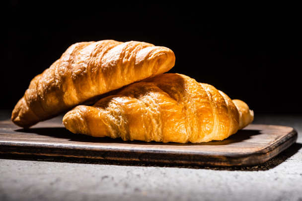 fresh baked croissants on wooden cutting board on concrete grey surface isolated on black - Foto, imagen