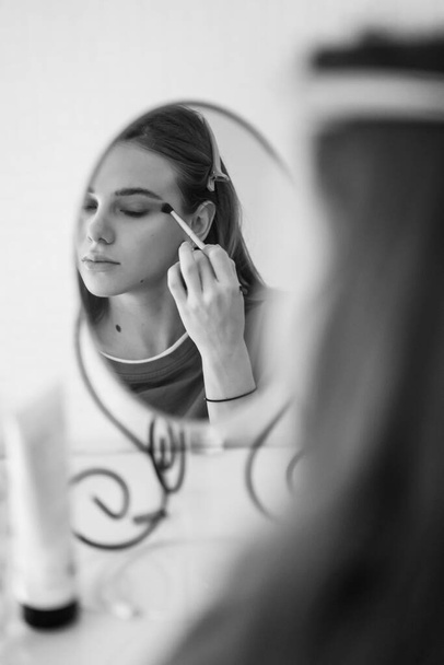 black-white. beautiful girl doing make-up and looks in the mirror. - Foto, afbeelding