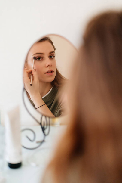 beautiful girl doing make-up and looks in the mirror. - Φωτογραφία, εικόνα