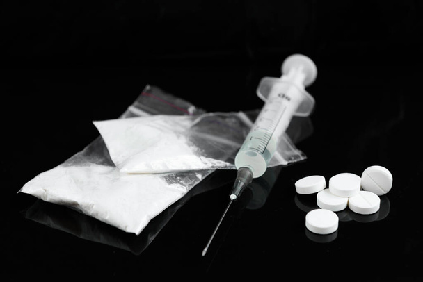 Медицинская концепция с крупным планом на двух шприцах, белые таблетки, ампулы, таблетки в упаковке другие препараты на черном глянцевом фоне
. - Фото, изображение