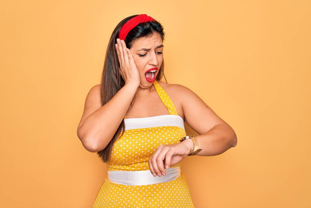 Young hispanic pin up woman wearing fashion sexy 50s style over yellow background Looking at the watch time worried, afraid of getting late - Fotó, kép